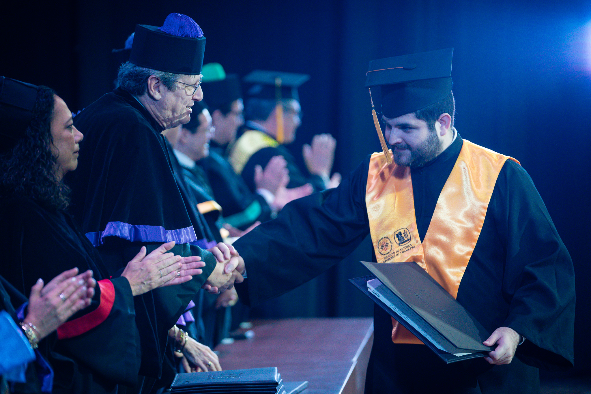 Basilio saluda y felicita a un chico de barba que se está graduando.