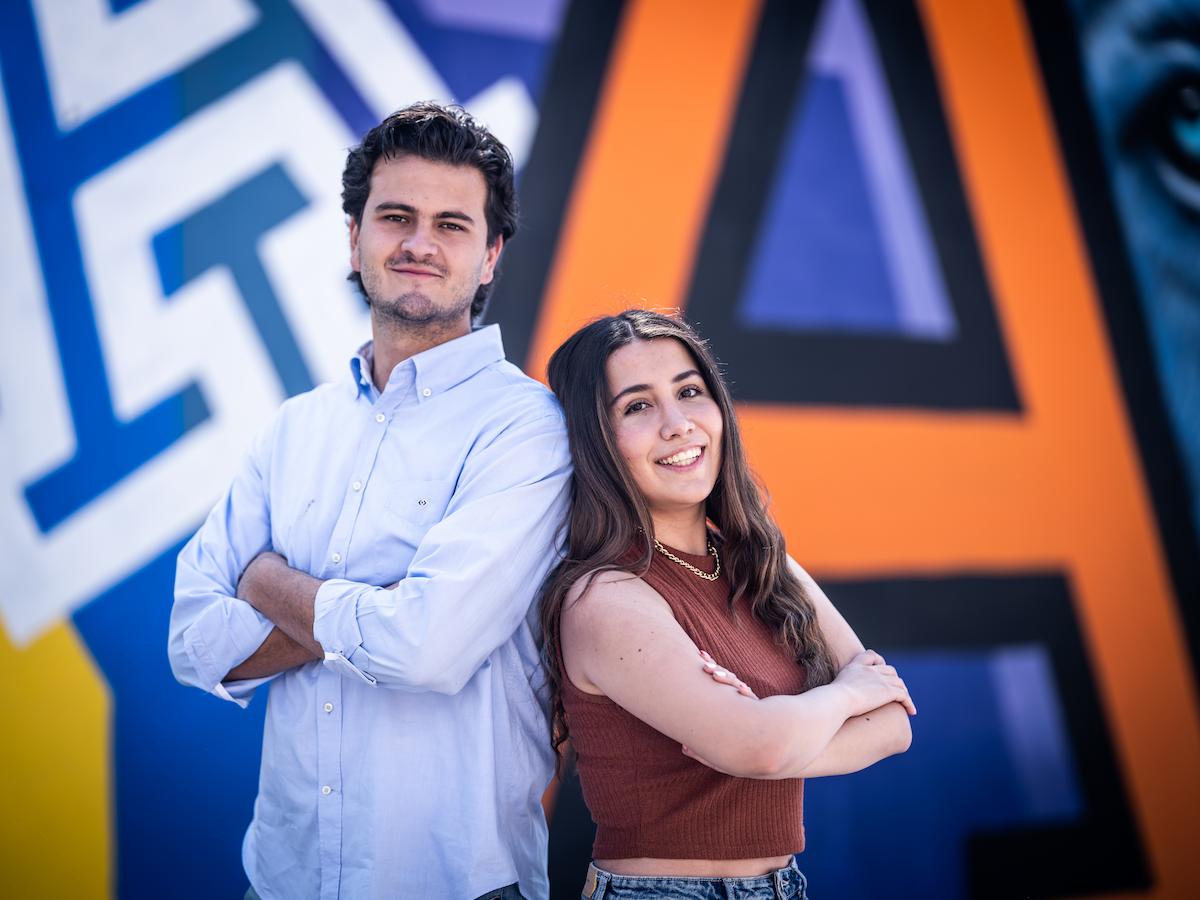 Dos estudiantes de licenciatura, con actitud segura y expresiva, frente a un mural artístico que resalta el ambiente creativo y moderno del campus Anáhuac.