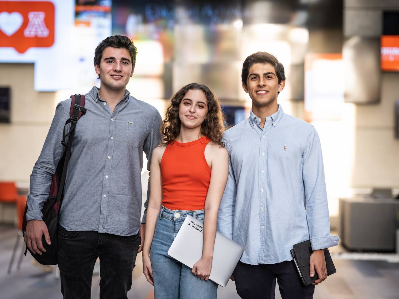 Grupo de tres estudiantes jóvenes con dispositivos electrónicos en mano, proyectando un ambiente académico dinámico en la Universidad Anáhuac.