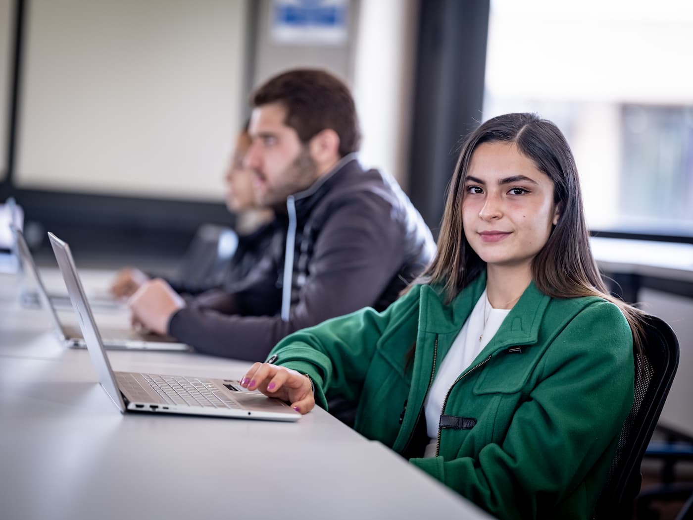 Estudiante sentada frente a su laptop en un aula, destacando por su actitud segura y profesional en un entorno académico de la Universidad Anáhuac.