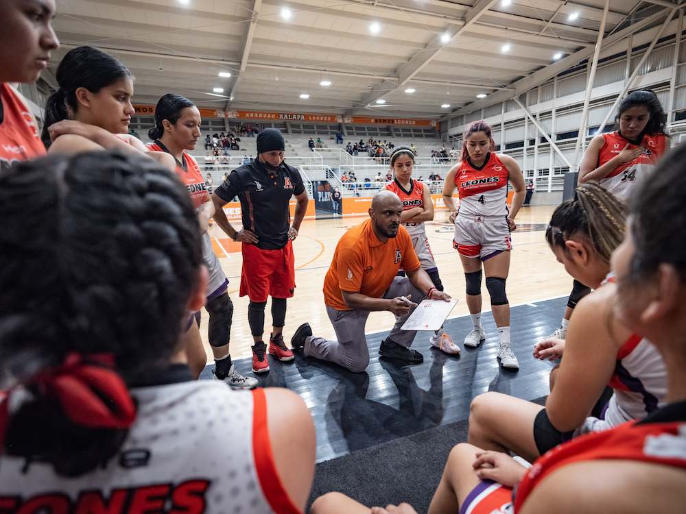 Entrenador de baloncesto dirigiendo a su equipo en una sesión de estrategia durante un partido.