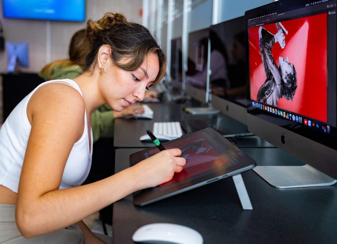 Dos estudiantes analizando datos en una laptop, con gráficos bursátiles proyectados al fondo, en un aula de la Universidad Anáhuac.