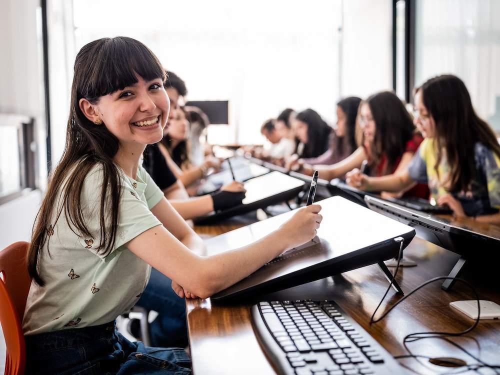 Estudiantes trabajando con tabletas gráficas en un aula de diseño digital, con una estudiante sonriendo mientras dibuja.