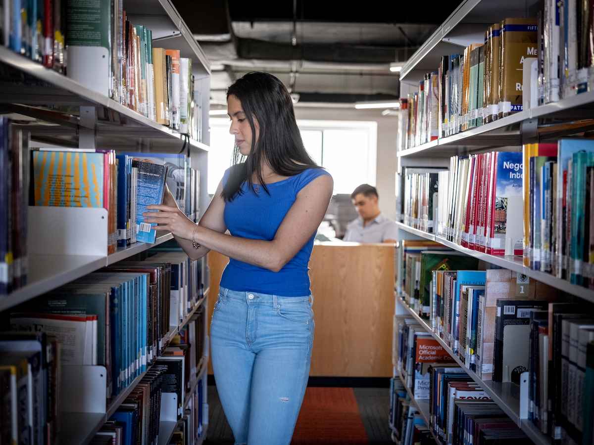Estudiante de Lenguas y Gestión Cultural consultando un libro en una biblioteca universitaria, reflejando el estudio de textos, la investigación cultural y el acceso al conocimiento.