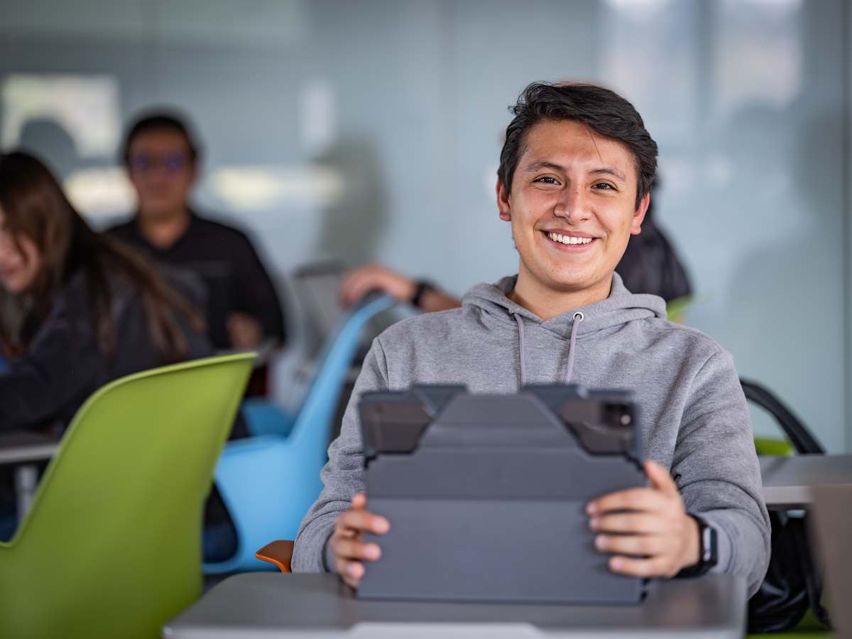 Estudiante de Pedagogía Organizacional y Educativa sonriendo mientras utiliza una tablet en el aula, reflejando formación pedagógica, uso de tecnología educativa y ambiente de aprendizaje positivo.